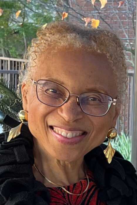 Dr. Allyson Yarbrough, in a black coat with gold earrings, smiles against a background of trees and a porch railing.