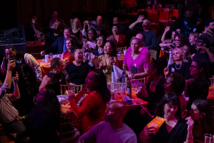 Rapt audience members sit at tables listening to GLIDE Holiday Jam 2025.
